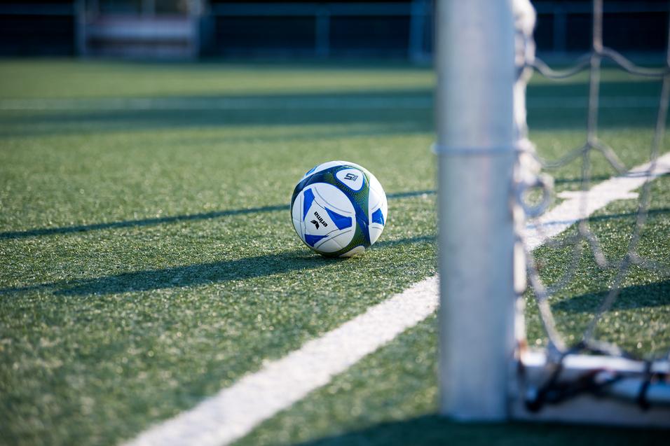 Fußball liegt auf einem Kunstrasenplatz, nahe einem Torpfosten mit Netz.