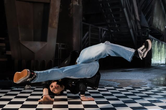 Tänzer führt einen Breakdance-Move auf einem schwarz-weißen Schachbrettboden durch, in einer modernen Umgebung.